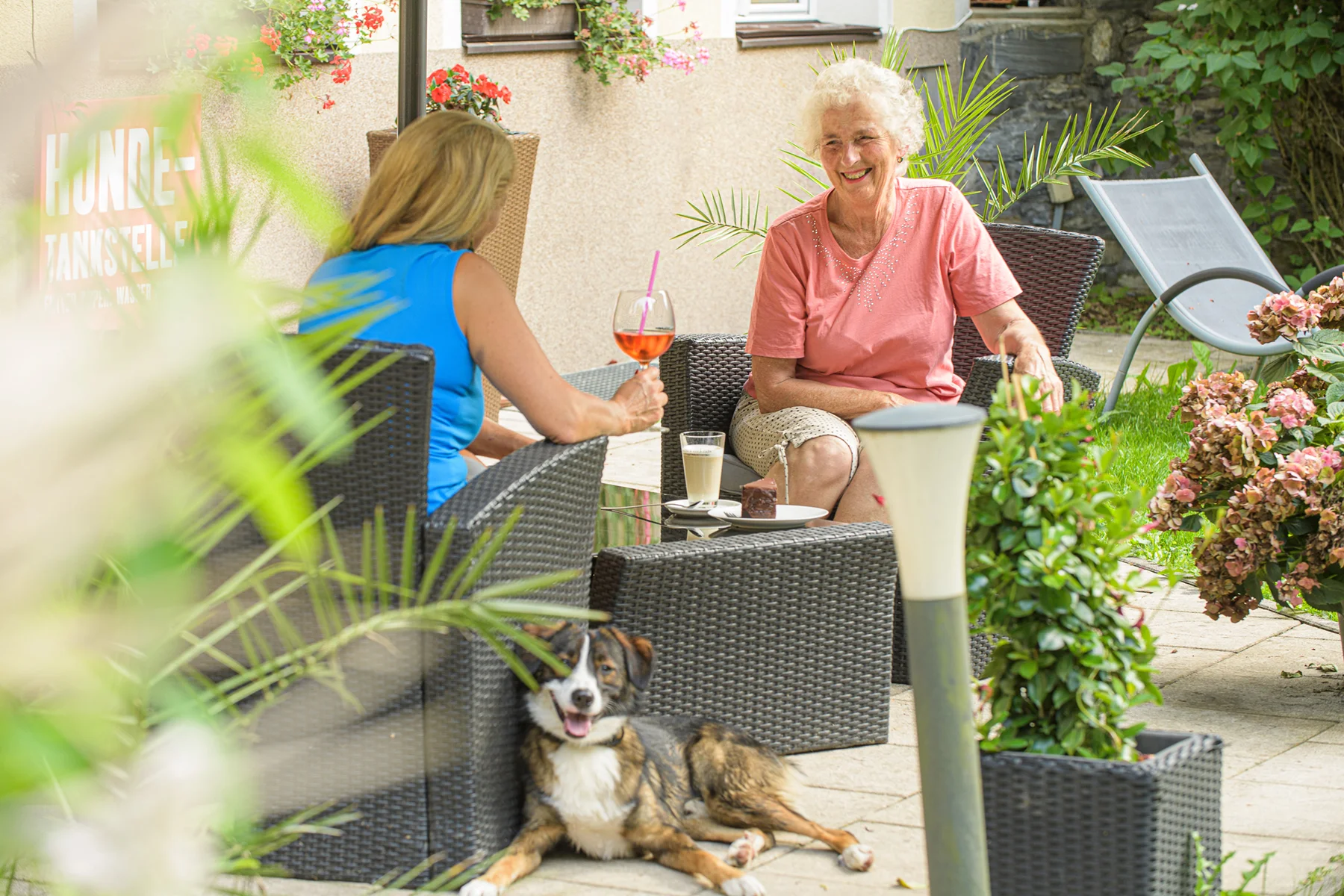 Ein Kurgast genießt Kaffee und Kuchen auf der Sonnenterrasse im GRUBERS Hotel-Apartments Gastein, während ein Hund entspannt daneben liegt – Kur mit Hund