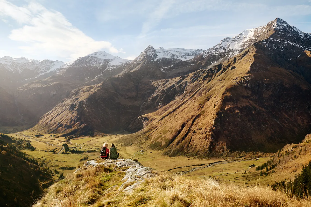 Zwei Frauen mit Blick über das Hochtal von Sportgastein mit herbstlicher Landschaft im Tal und schneebedeckten 3000ern im Hintergrund